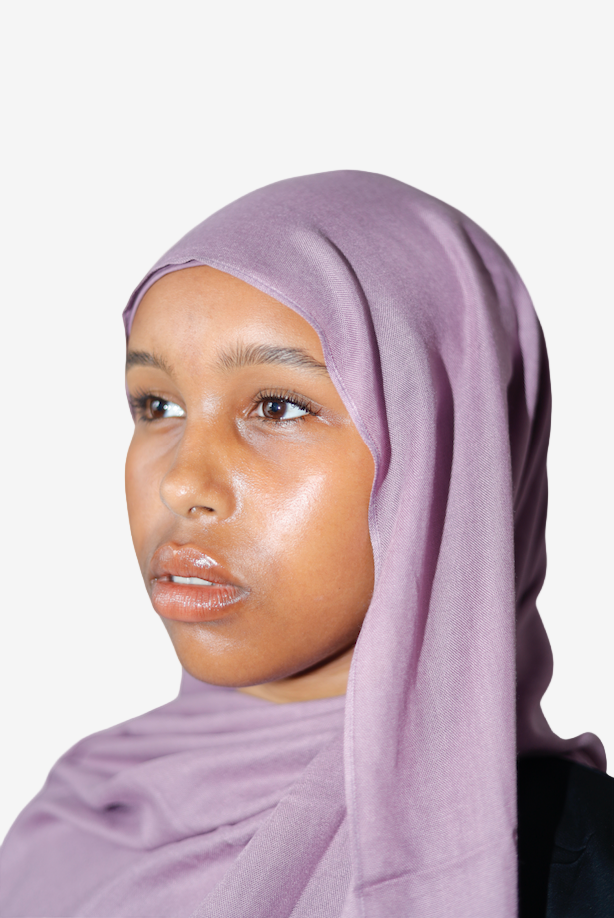 Woman wearing a light purple hijab against a plain background